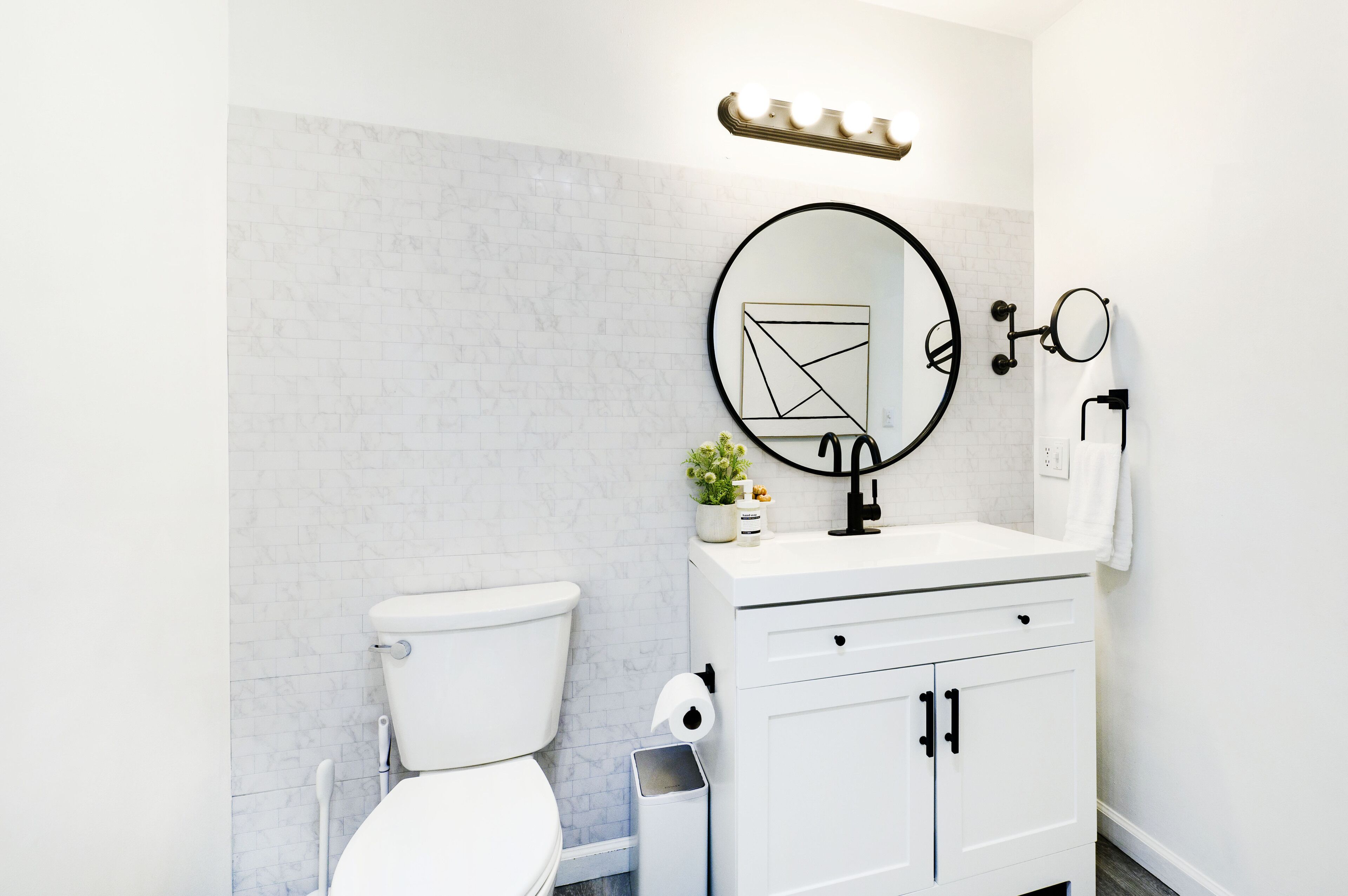 Un bagno moderno con il water bianco, un lavandino con specchio e un cestino.