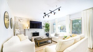Een moderne woonkamer met een witte bakstenen haard, witte banken, een bijzettafeltje en een flatscreen televisie die boven de haard hangt.