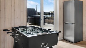 Una taula de futbolí a una habitació amb un frigorífic gran i vistes a una terrassa amb places a l'aire lliure.