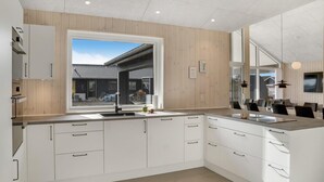 Una cuina moderna amb armaris blancs, un finestral gran i vista a una zona residencial.