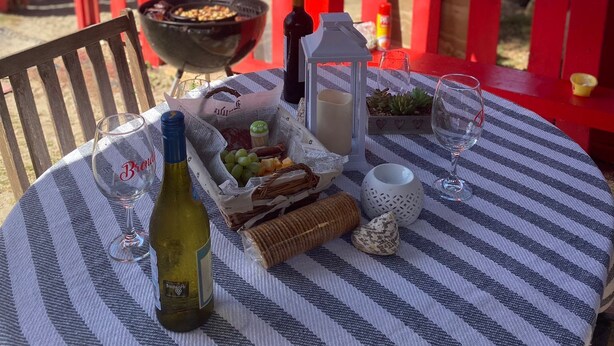 A table set with a bottle, glasses, and snacks on a striped tablecloth, overlooking a beach with red railings and palm trees. - Studio facing the sea and only 15 minutes from the public ferry (Fajardo)
