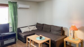 A living room with a sofa, a TV, a small table, a lamp, and an air conditioner.