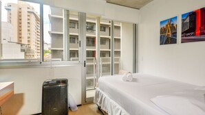 A hotel room with a bed, a radiator, a window with a view of buildings, and a door leading to a balcony. - OBA 142 - Super Estúdio Frei Caneca (São Paulo)