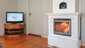 A room with a fireplace, a television on a wooden stand, and patterned wallpaper. - Stunning home in Södra Vi with kitchen (Södra Vi)