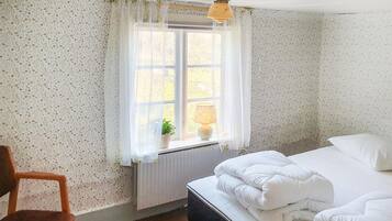 Ett sovrum med en säng, en stol, ett fönster med gardiner och en lampa.