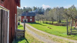 A red house with a gravel path leading to it, surrounded by trees and a wooden structure to the right. - Stunning home in Södra Vi with kitchen (Södra Vi)