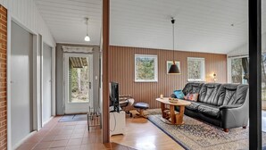 A spacious living room with a black leather sofa, a wooden coffee table, and a television. There are two windows providing natural light and a view of the outdoors. - Beautiful home in Herning with WiFi (Herning)