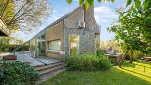 Ein modernes Haus mit Steinaußenwand, Glastür und einer kleinen Sitzgelegenheit im Freien.
