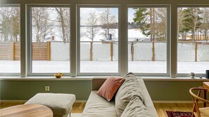 Ett rum med ett stort fönster, en soffa, ett träbord och en stol.