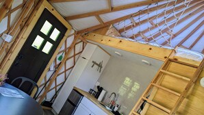 A compact kitchen with a wooden ceiling, a dining area with a table and chairs, and a small refrigerator. - Luxury Glamping Yurt with Loft, Wood-Fired Hot Tub (Sears)