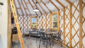 A cozy room with a wooden lattice wall, a sofa, a dining table with chairs, and a ladder. - Luxury Glamping Yurt with Loft, Wood-Fired Hot Tub (Sears)