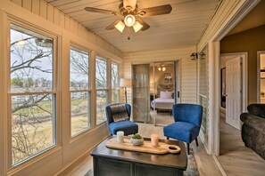 Une pièce chaleureuse avec un ventilateur de plafond, de grandes fenêtres, une table basse en bois décorée de bougies et une vue sur l’extérieur.