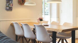 Zona pranzo con tavolo di legno e sedie grigie, un vaso con fiori e due lampade a sospensione.