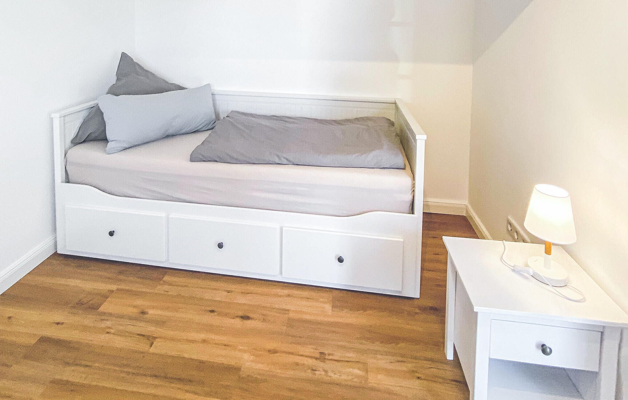 Una camera da letto piccola e ordinata, con un letto singolo, un comodino e una lampada.
