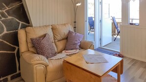 Un salón acogedor con un sofá, dos almohadas, una mesita y vistas a una terraza exterior.