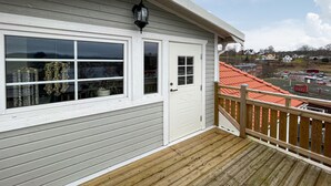 Una terraza de madera con una puerta y ventanas blancas que dan a un barrio residencial con casas de techo rojo.