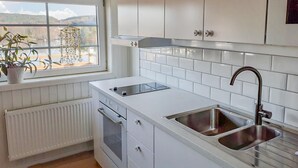 Una cocina moderna con armarios blancos, horno empotrado, pileta doble y ventana con vista a las colinas.