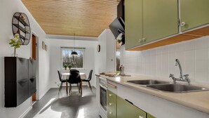 Una cocina moderna con techo de madera, zona de comedor con mesa y sillas, y armarios verdes.