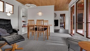 Una sala de estar moderna con un sofá de cuero negro, una mesa de comedor de madera y sillas. Hay una estantería con libros y objetos decorativos, y un ventanal con vistas al exterior.