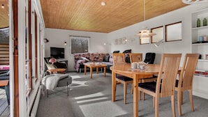 Una sala de estar acogedora con techo de madera, un sofá, una mesa de comedor con sillas y una televisión.
