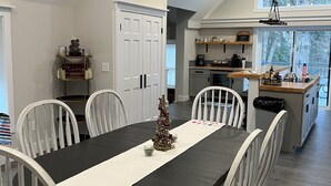 Un comedor con una mesa larga, sillas blancas y un centro de mesa con un árbol de Navidad.