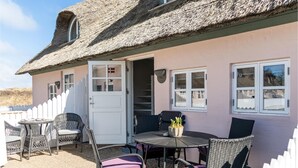 A house with a thatched roof, a white door, and a small patio area with wicker furniture and a table. - Stunning home in ålbæk with WiFi (Ålbæk)