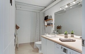 Un baño moderno con inodoro, lavabo y lavadora Bosch. Hay plantas en la encimera del lavabo y una cortina de ducha con diseño geométrico.