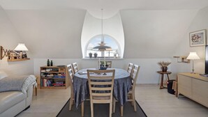 A dining area with a round table, chairs, a bookshelf, a sofa, and a window with a view. - Stunning home in ålbæk with WiFi (Ålbæk)