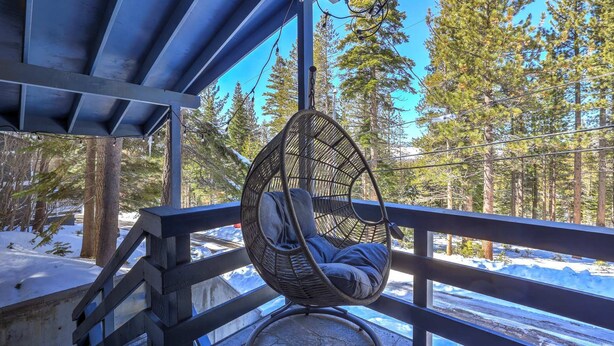 A hanging chair on a balcony with a view of snow-covered ground and pine trees. - Southern Pines Arcade Games & Foosball for Kids! (South Lake Tahoe)