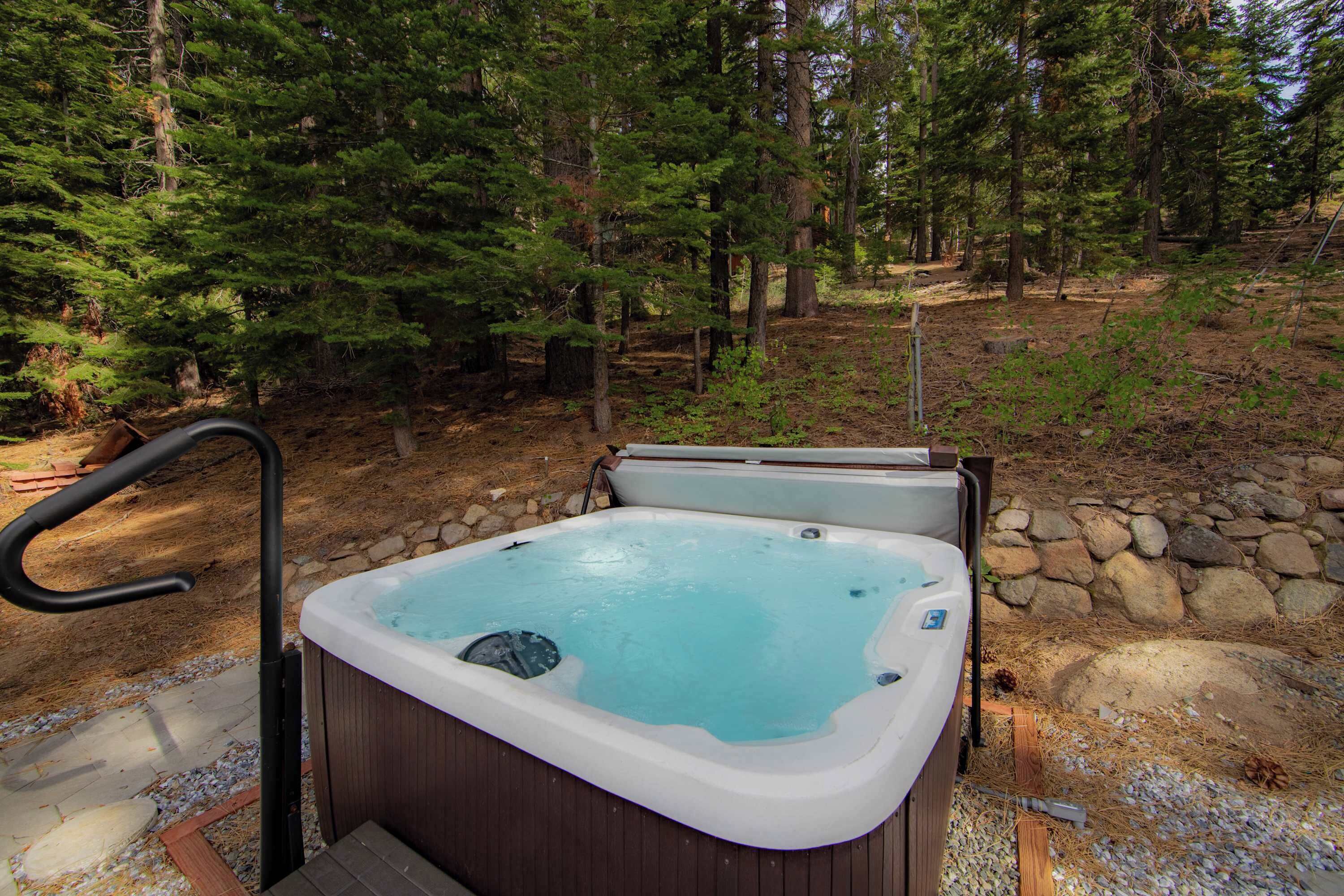 Ein Whirlpool inmitten von Bäumen, mit einer Holzterrasse und einer Steinmauer.