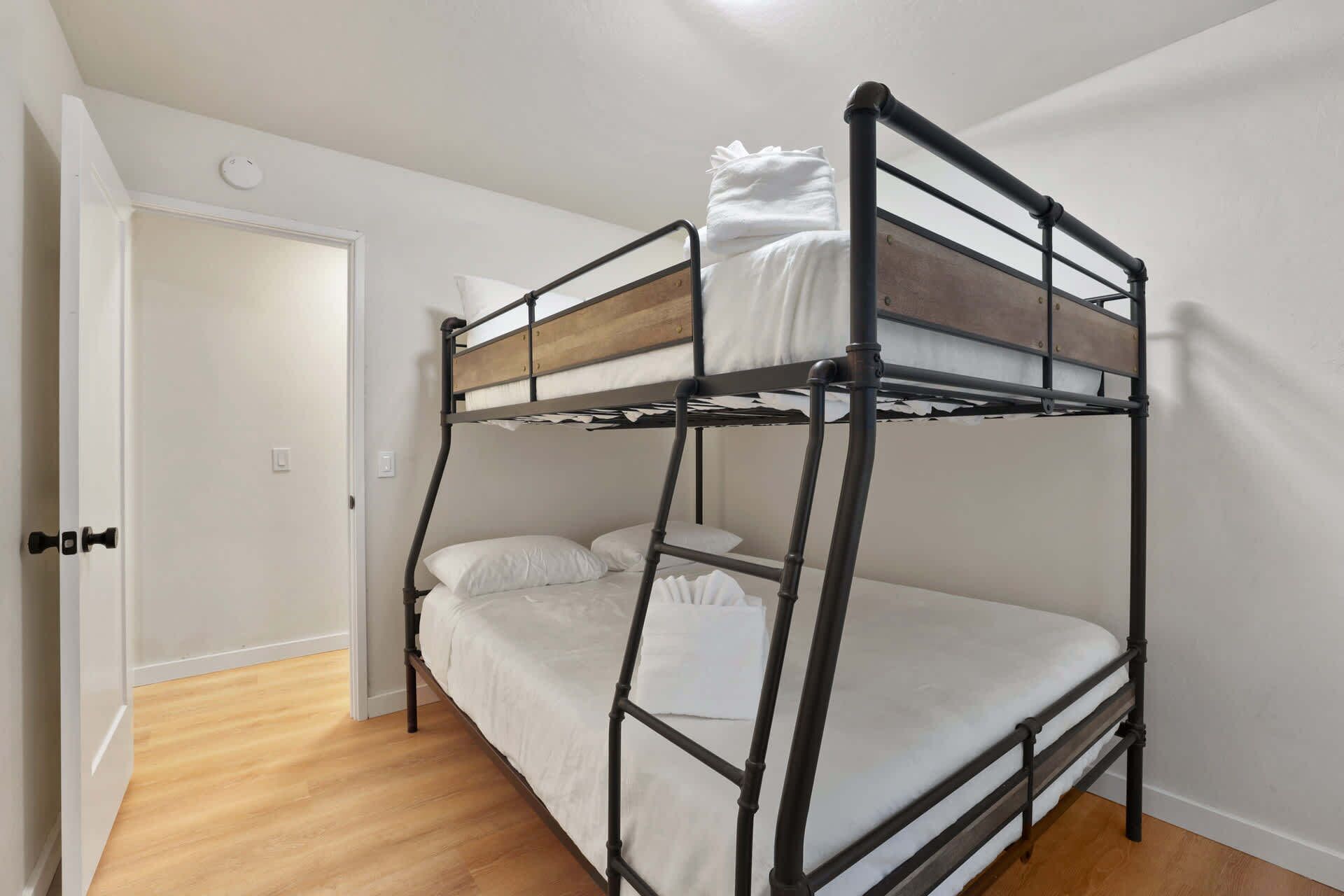 Un lit superposé avec une tête de lit en bois, une literie blanche et une porte sur le côté gauche.