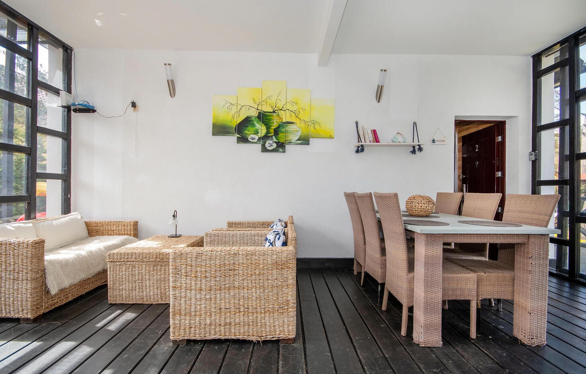 A modern living room with wicker furniture, a dining table, and a painting on the wall.