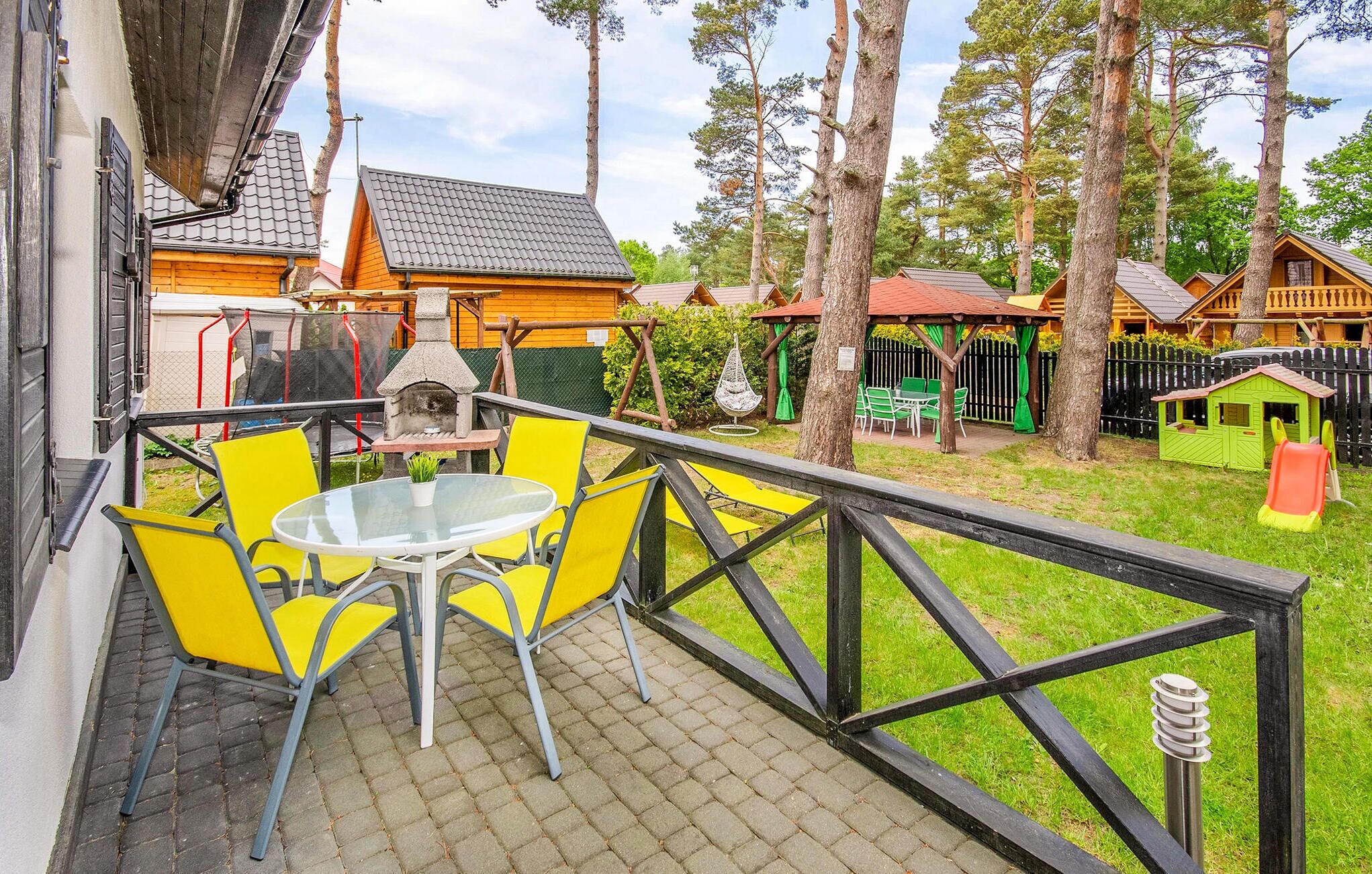 A patio with yellow chairs and a table, surrounded by wooden fences and trees.