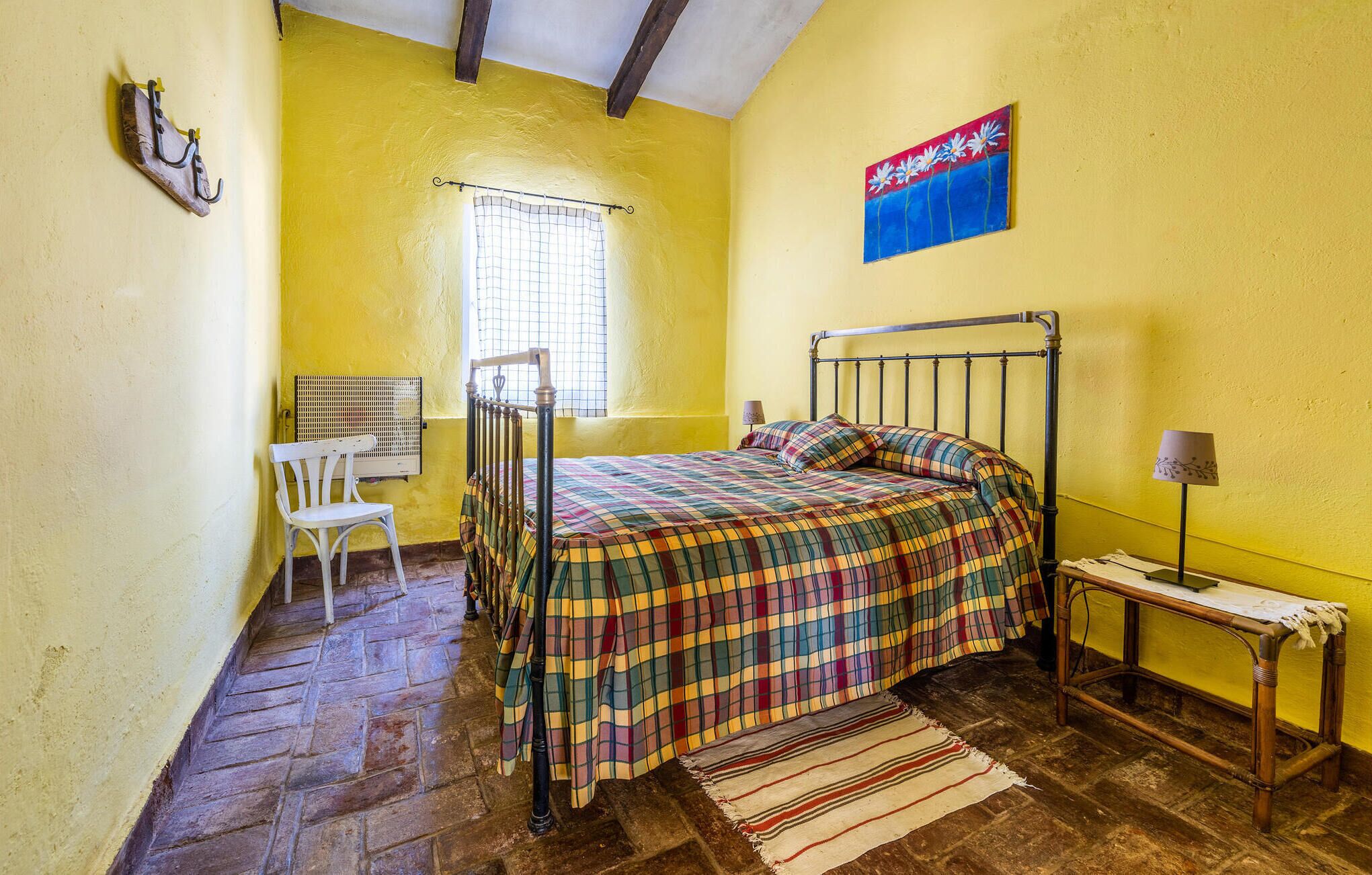 Habitació amb llit, cadira, taula petita i finestra.