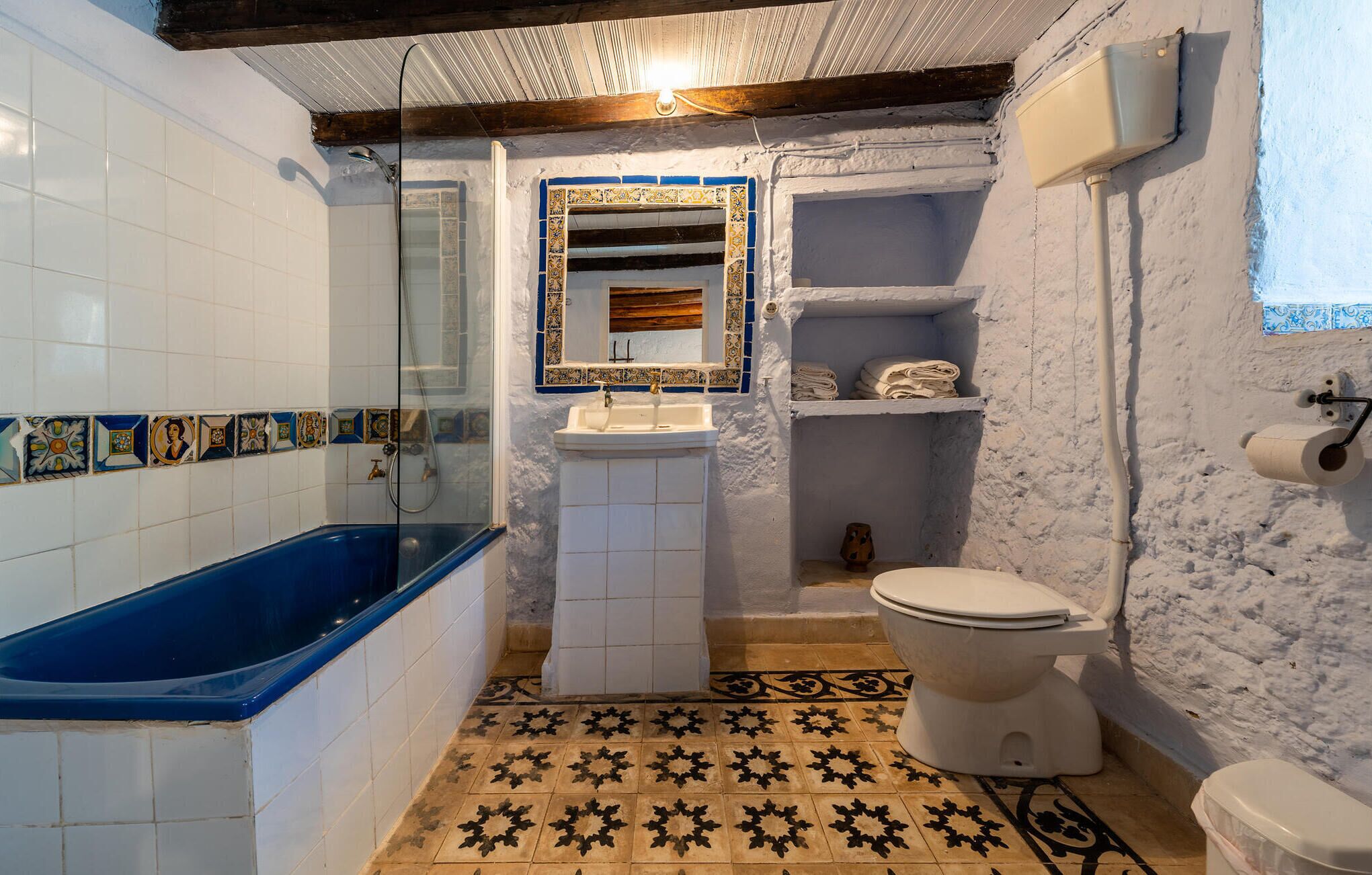 Un baño con bañera, lavamanos, inodoro y un pequeño estante con toallas.