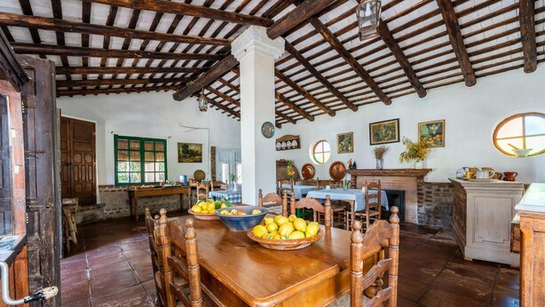 A rustic dining room with a wooden table and chairs, a fireplace, and various kitchen items.