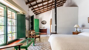 A room with a bed, a green chair, a wooden table, a mirror, and a patterned floor.