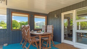 Eine überdachte Terrasse mit einem Holztisch und Stühlen, großen Fenstern und einer Glastür.