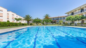 En swimmingpool med klart, blåt vand, omgivet af velplejede grønne områder og bygninger med altaner.