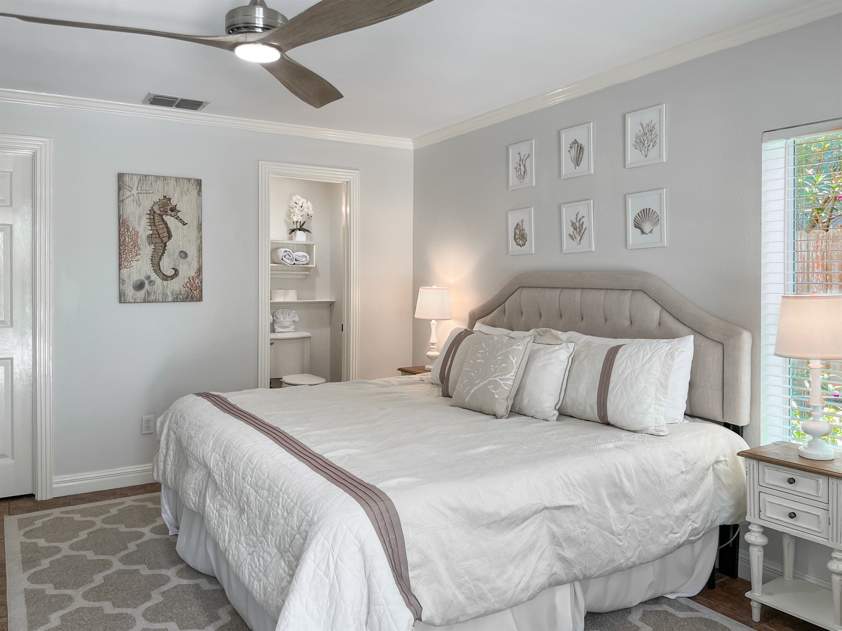 A neatly arranged bedroom with a bed, bedside tables, a ceiling fan, and a window with blinds.