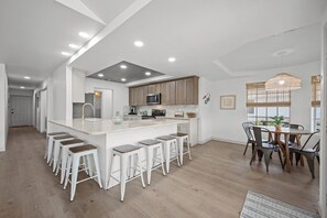 A modern kitchen with a central island, bar stools, and a dining area with a table and chairs.