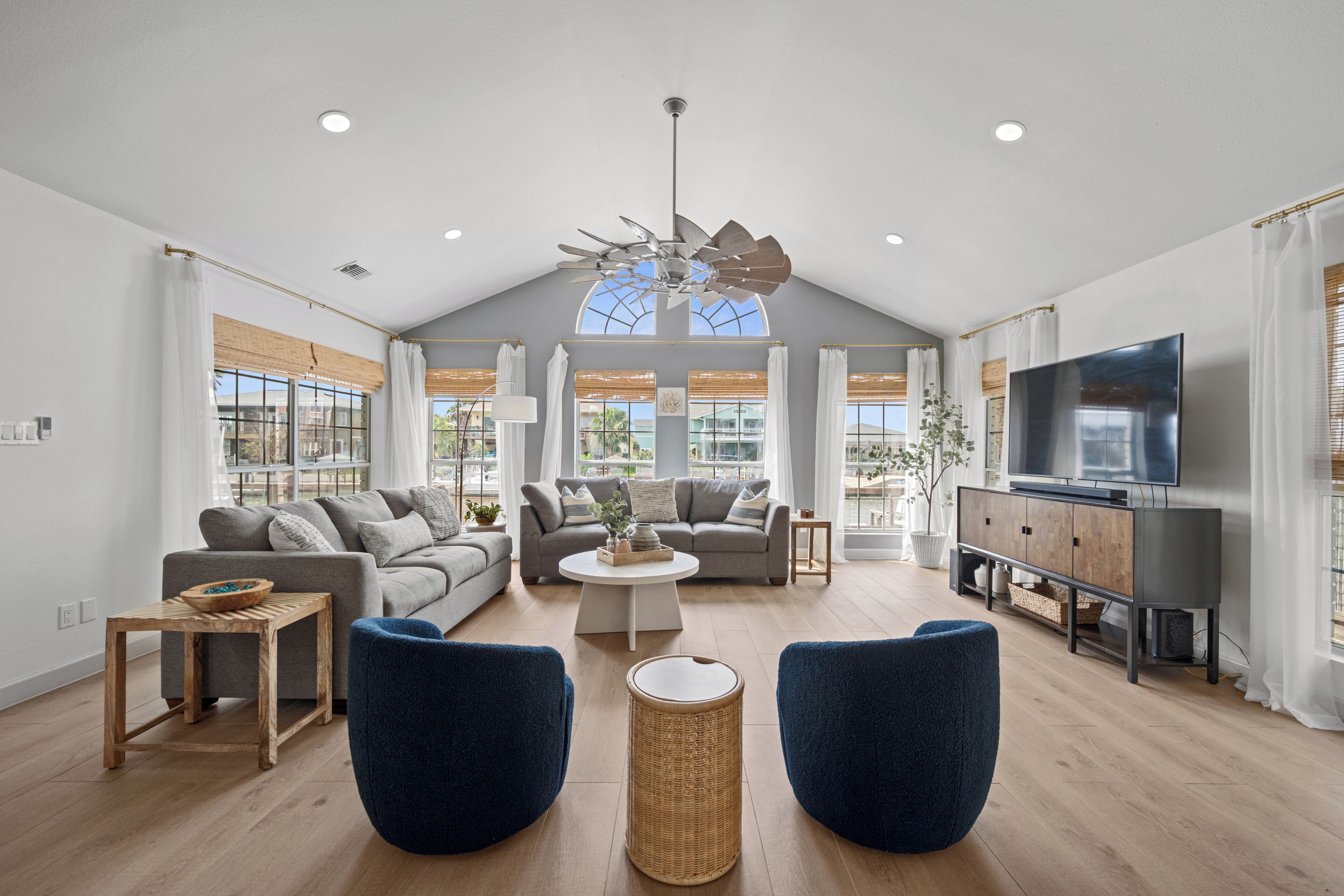 Un salon spacieux avec un plafond haut, un grand téléviseur et un ventilateur de plafond.