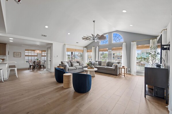 A spacious living area with a high ceiling, large windows, and a modern ceiling fan.