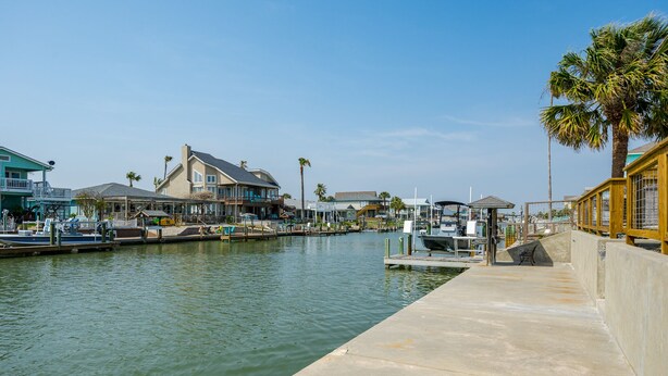 A marina with boats docked, a concrete walkway, and buildings with balconies and palm trees. - NEWLY REMODELED - Rockport Waterfront Oasis (Rockport)