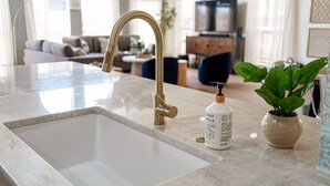 A modern kitchen with a marble countertop, a gold faucet, and a potted plant. - NEWLY REMODELED - Rockport Waterfront Oasis (Rockport)