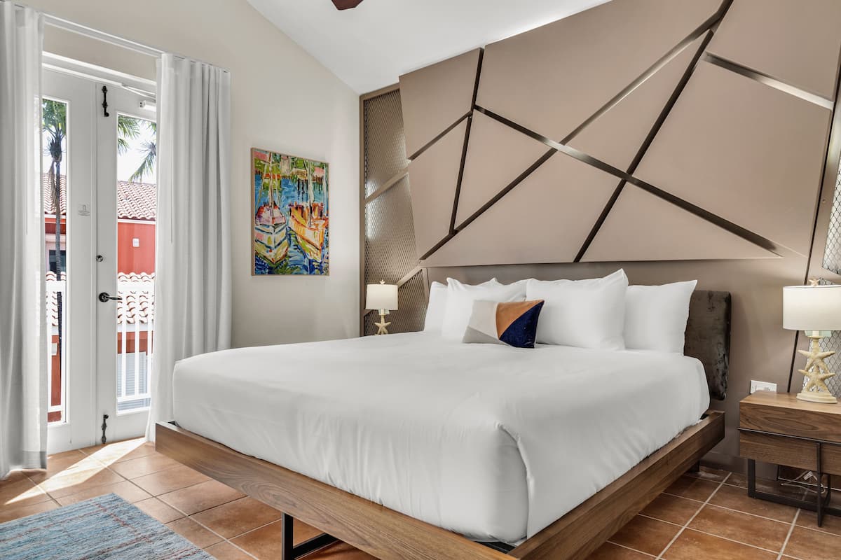 Una cama grande con estructura de madera, una pared con diseños geométricos y un cuadro de colores en la pared.