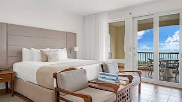Habitación de hotel con una cama grande, una silla de madera, una mesita pequeña y un balcón con vistas.