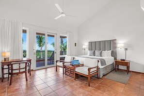 A bedroom with a bed, a desk, a chair, a nightstand, and a balcony with a view of palm trees. - Las Casitas Village at El Conquistador (Fajardo)