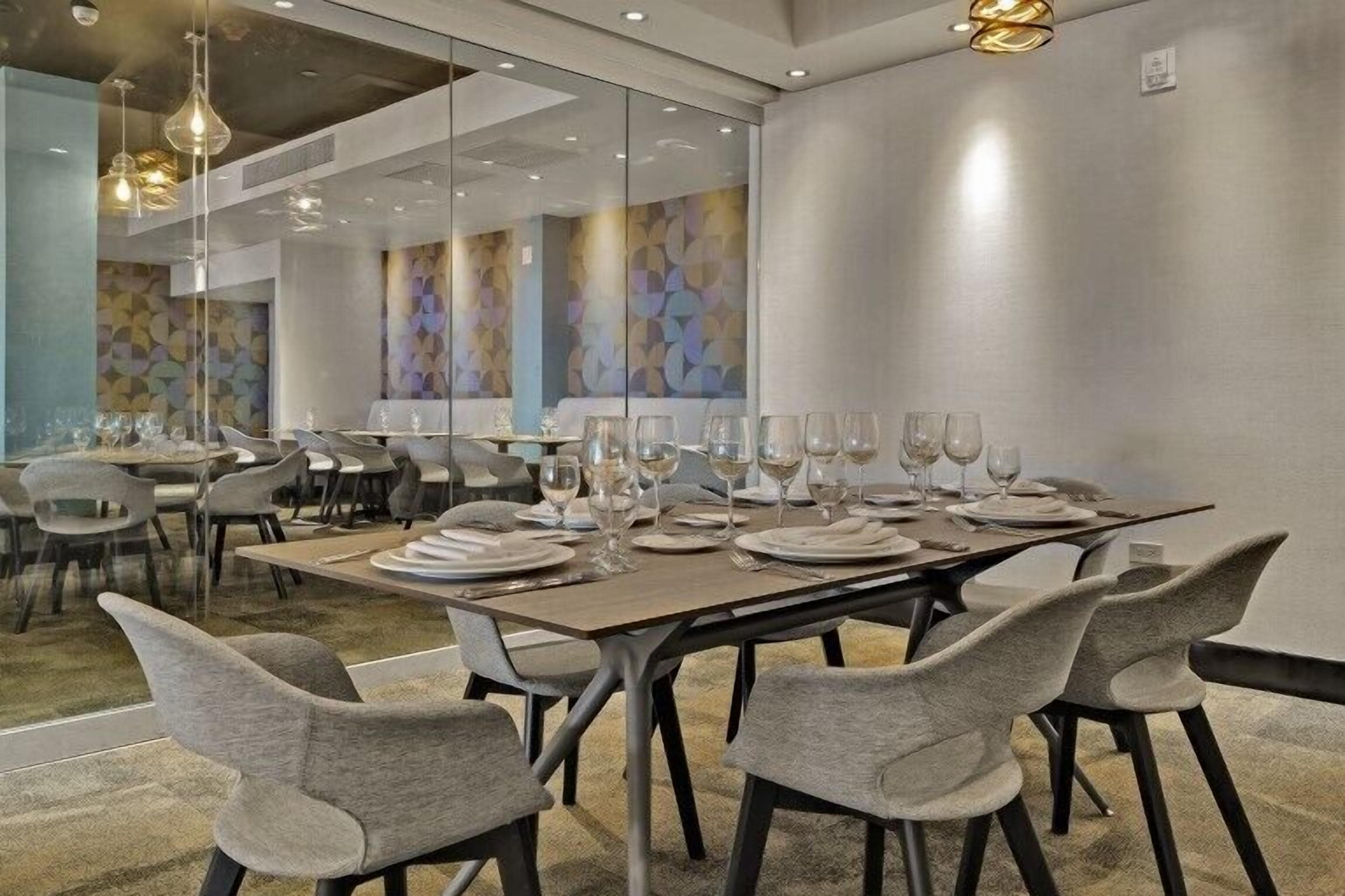 A modern dining area with a long table set for a meal, surrounded by grey upholstered chairs.