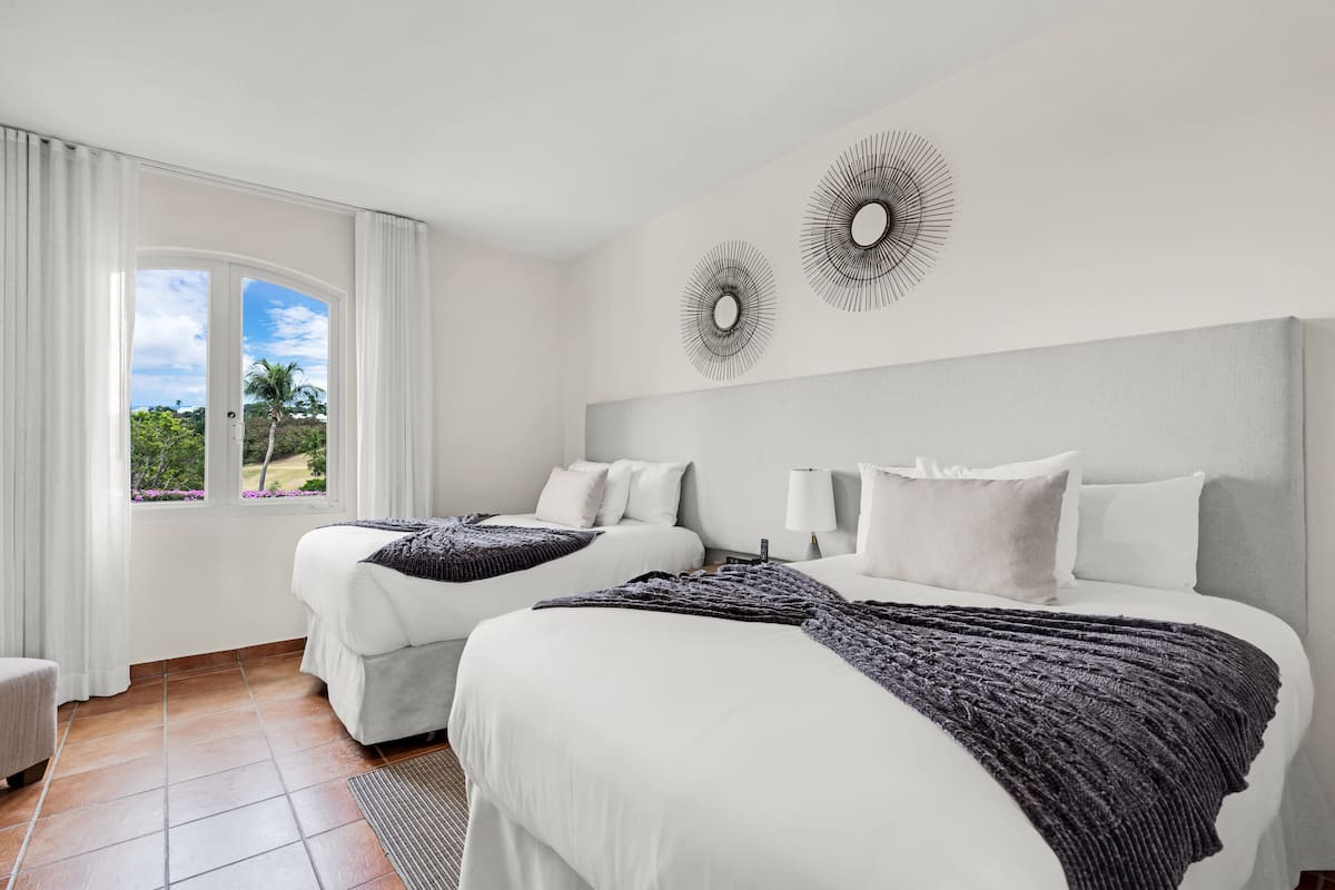 Habitación de hotel con dos camas, un ventanal con cortinas y una obra de arte en la pared.